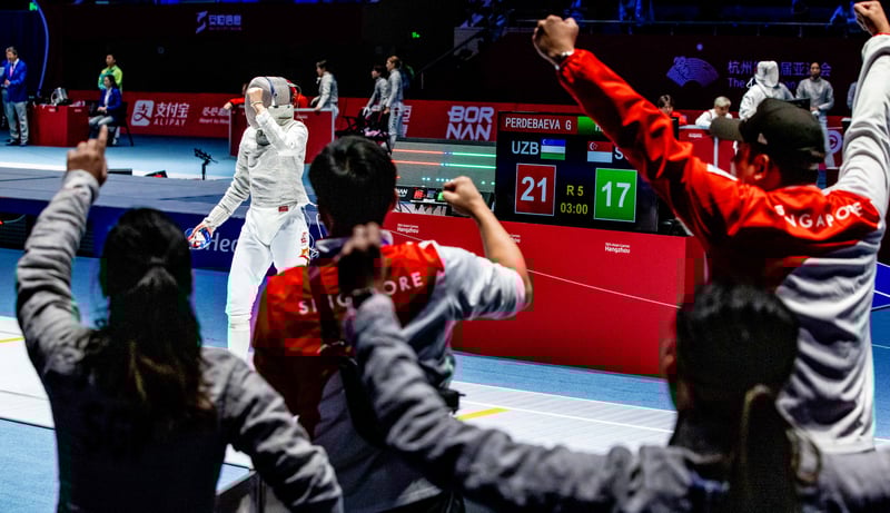 Juliet Heng celebrates scoring a point against her Uzbekistan opponent in front of her team mates in the women’s team sabre event. (Photo: SNOC/ Kelly Wong)

