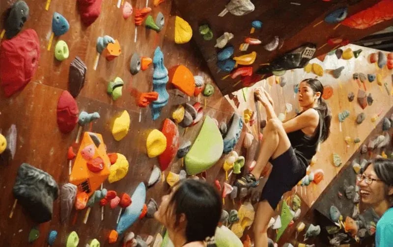 Woman doing bouldering at OYEYO Boulder Home with onlookers