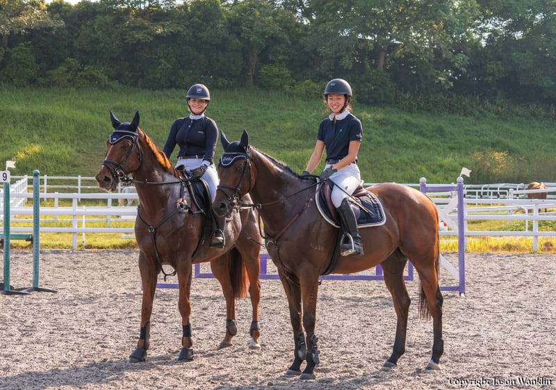 Two ladies wearing black riding on brown horses