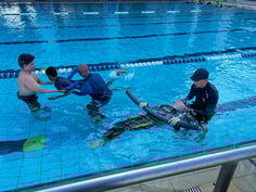 Photo of Para Sport Academy two swim coaches guiding two learners in the swimming pool using floatation aids known as noodles