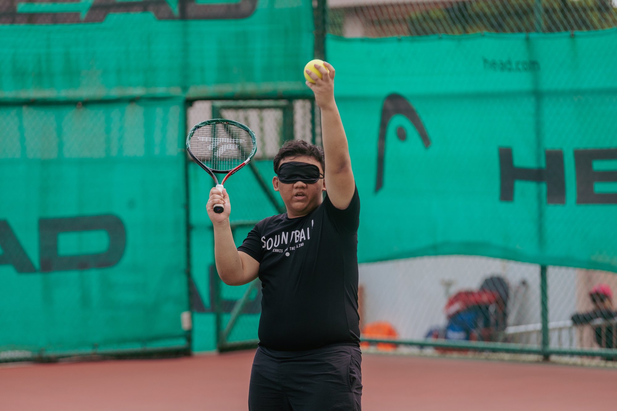 Photo of a male learner wearing cloth shades over his eyes preparing to hit a Soundball ball with a tennis racket