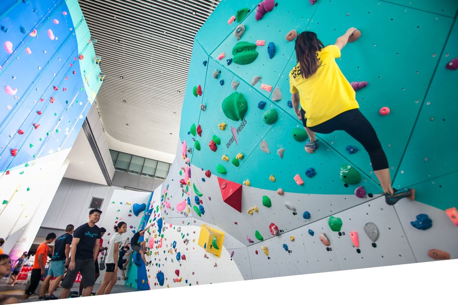 Lady wearing a yellow shirt doing rock climbing at The Rock School